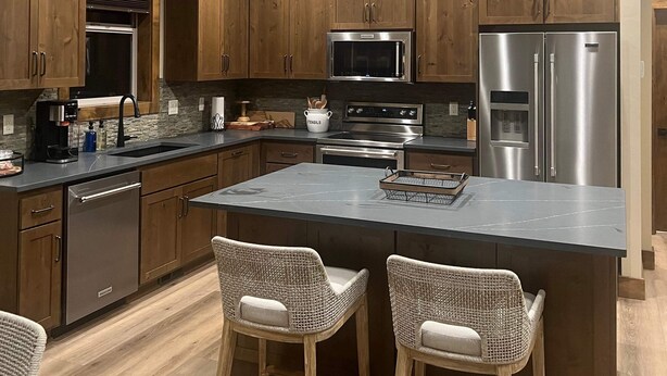 A modern kitchen with wooden cabinets, stainless steel appliances, and a central island with bar stools. - Newer 3-bedroom cabin in fantastic Two Rivers North, free WiFi (Crescent Lake)