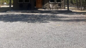 A two-story wooden cabin with large windows, a covered porch, and a gravel driveway. - Newer 3-bedroom cabin in fantastic Two Rivers North, free WiFi (Crescent Lake)