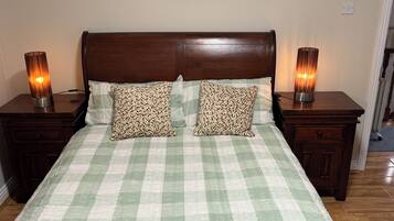 A neatly made bed with a checkered bedspread, two patterned pillows, and two bedside lamps on wooden nightstands.