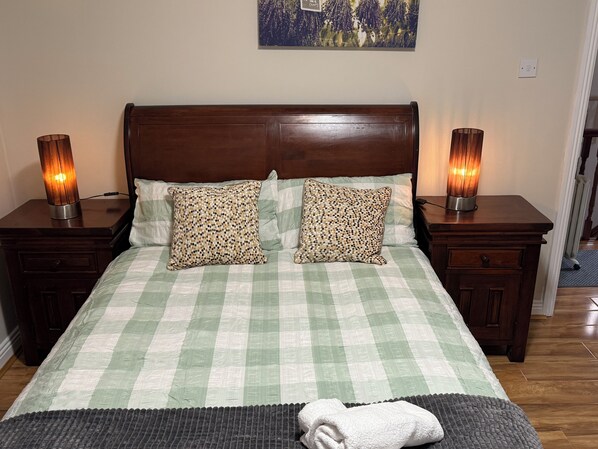 A neatly made bed with a checkered bedspread, two patterned pillows, and two bedside lamps on wooden nightstands. - The Meadow House Cobh (Cobh)