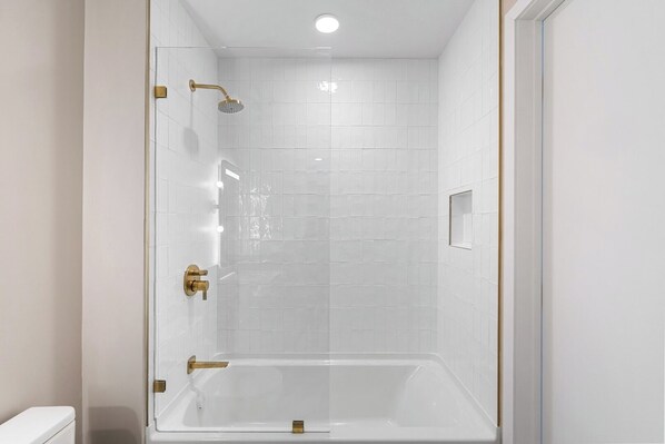 Un baño moderno con ducha envuelta en vidrio, paredes con azulejos blancos y una bañera blanca.