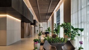 Un interior moderno con un largo pasillo, plantas en macetas y zonas de descanso.