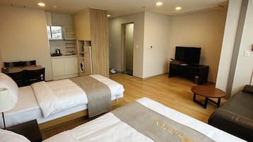 Una habitación de hotel con dos camas, televisión, una kitchenette pequeña y baño.