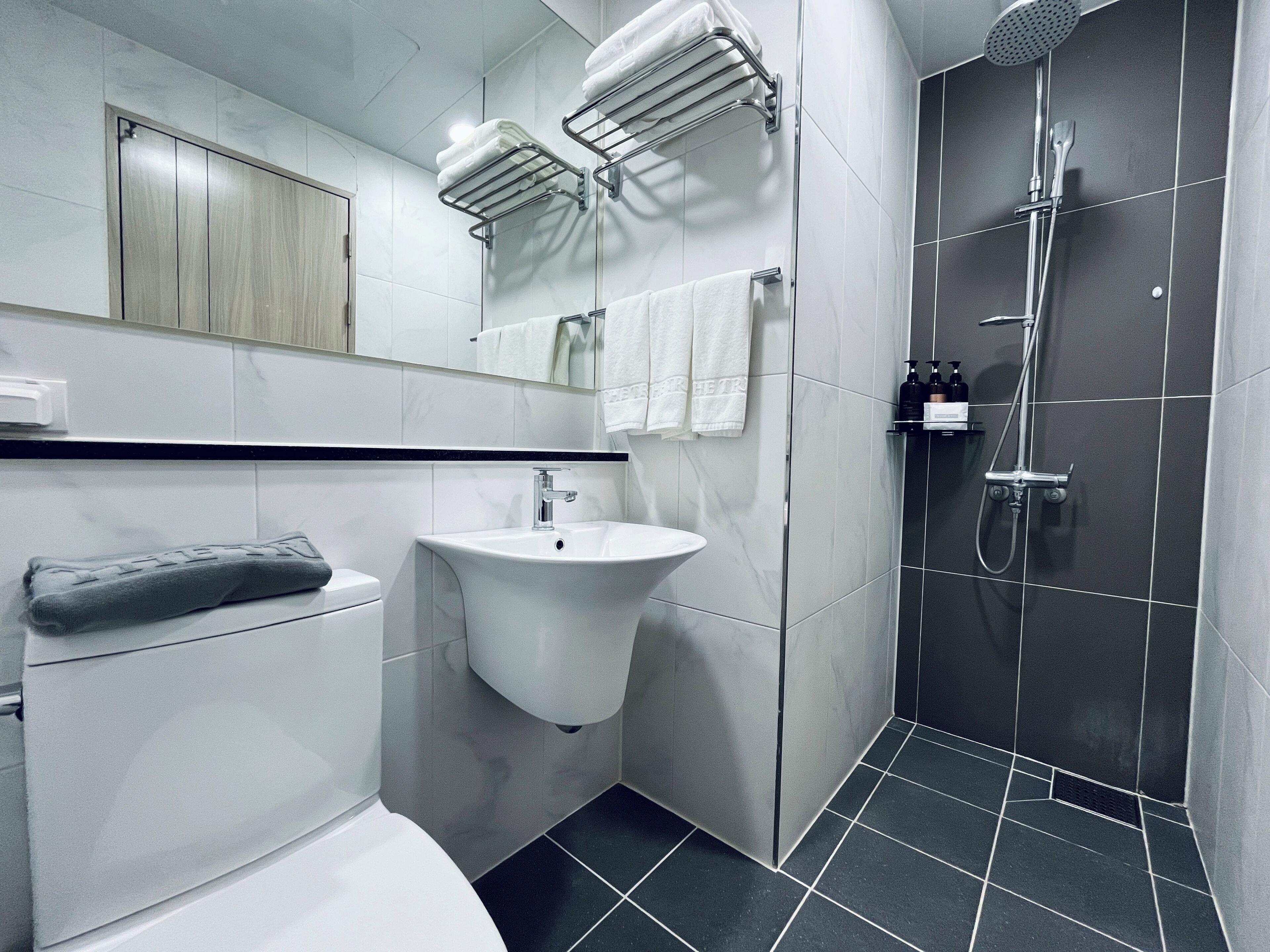 A modern bathroom with a toilet, sink, towel rack, and shower.