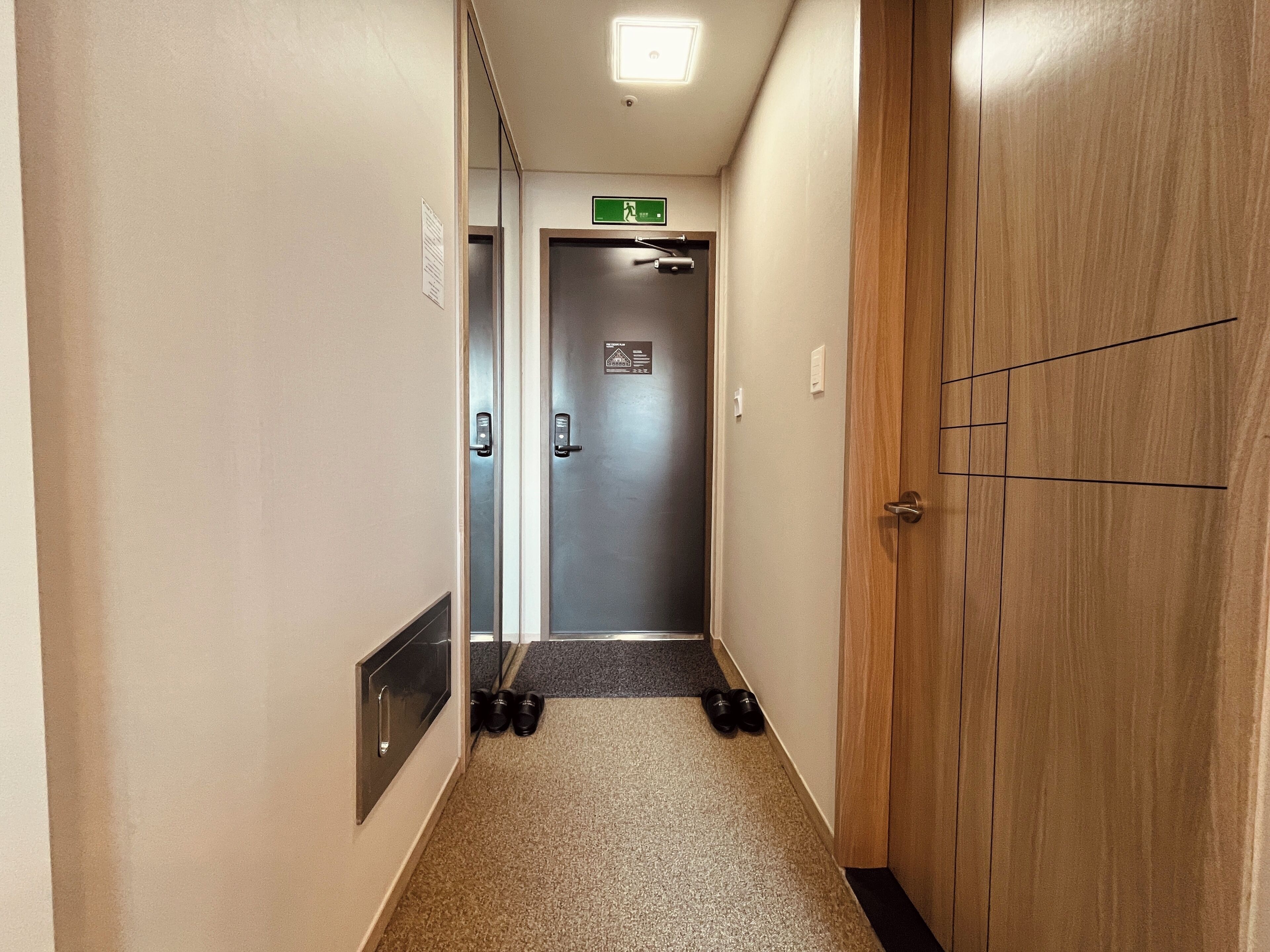 A narrow hallway with a wooden door on the right and a metal elevator door at the end.