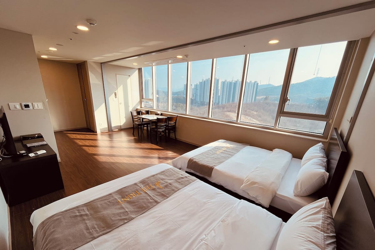A hotel room with two beds, a desk with a computer, and a dining area with chairs.