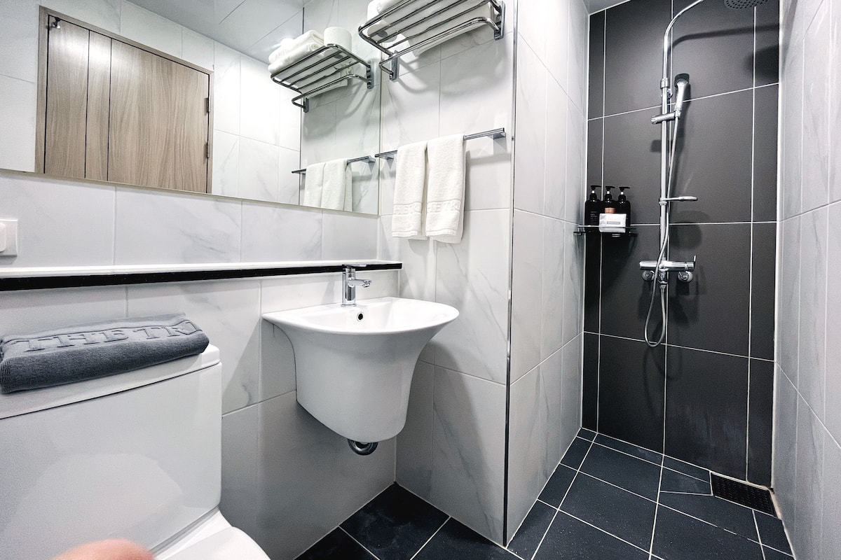 A modern bathroom with a sink, towel racks, a shower, and a wooden cabinet.