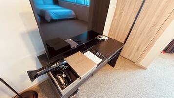 A hotel room with a large flat-screen TV, a wooden desk, and a small sink with a towel.