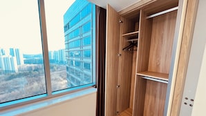 Ein Zimmer mit großem Fenster, Holzschrank und Blick auf hohe Gebäude.