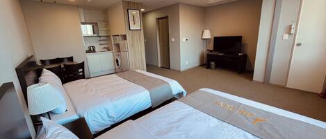 A hotel room with two beds, a desk, a TV, a washing machine, and a kitchenette.