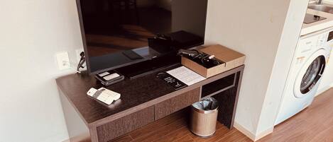 A modern living room with a flat-screen TV, a coffee table, a small trash bin, and a washing machine in the background.