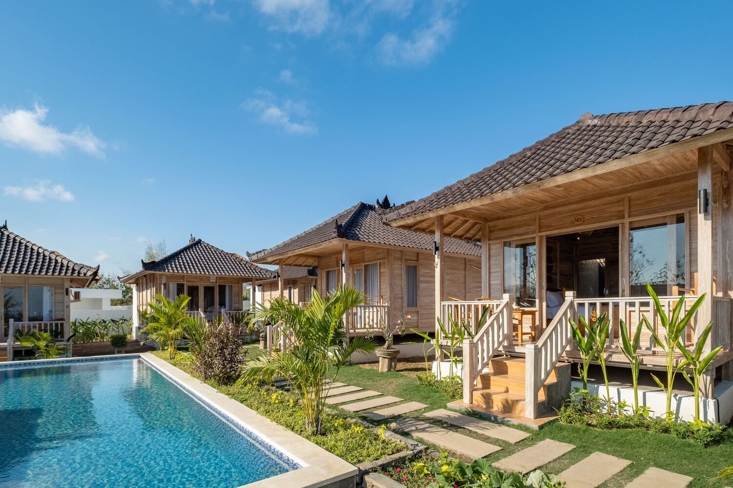 A row of wooden cabins with tiled roofs, a swimming pool, and a well-maintained garden.