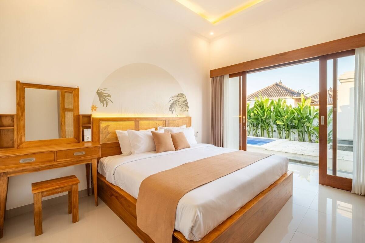 Un dormitorio moderno con una cama grande, muebles de madera, un espejo amplio y vistas a una piscina y vegetación.
