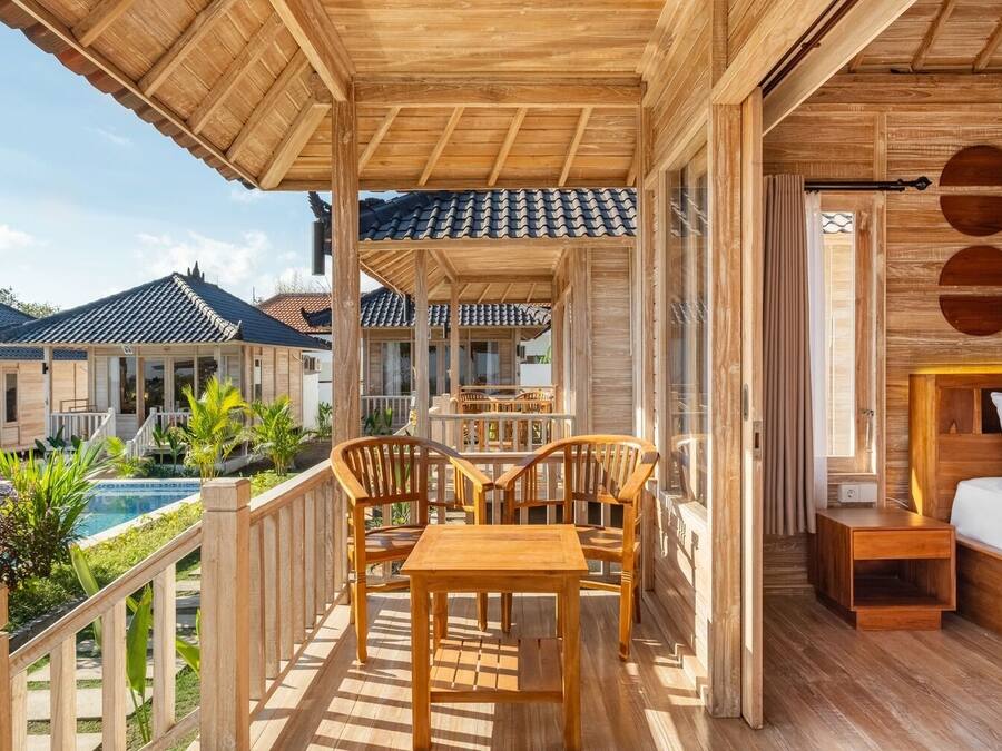 Un balcón de madera con una mesa y sillas, con vista a una piscina y otros edificios.