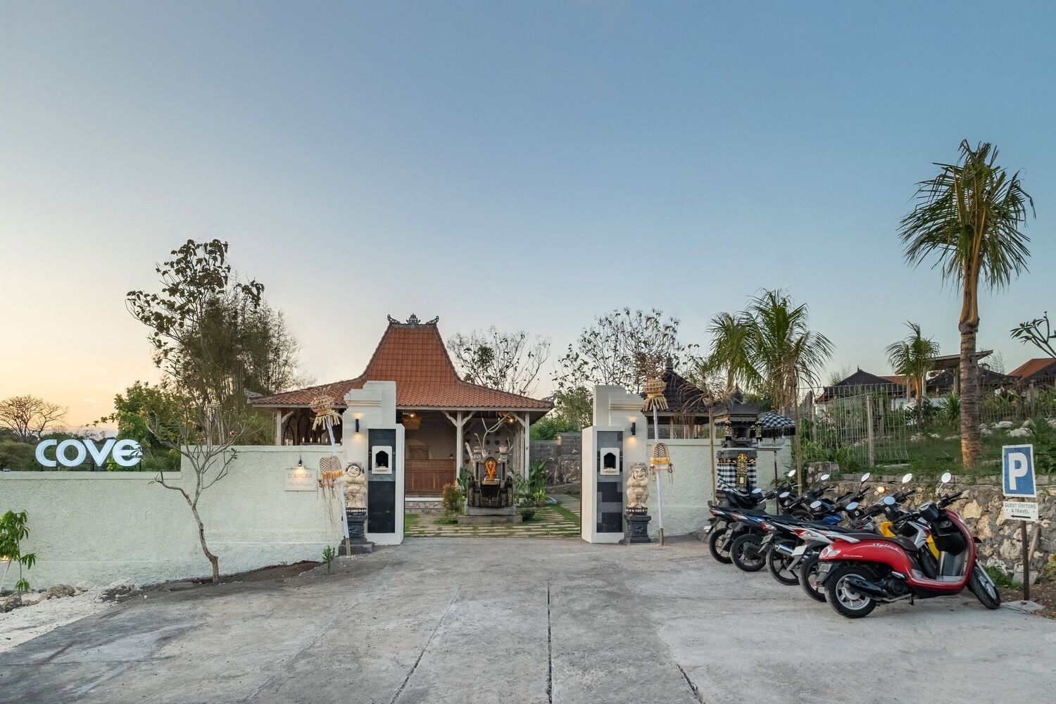 A gated entrance with a traditional roof, a sign reading "Cove", and several motorcycles parked outside.