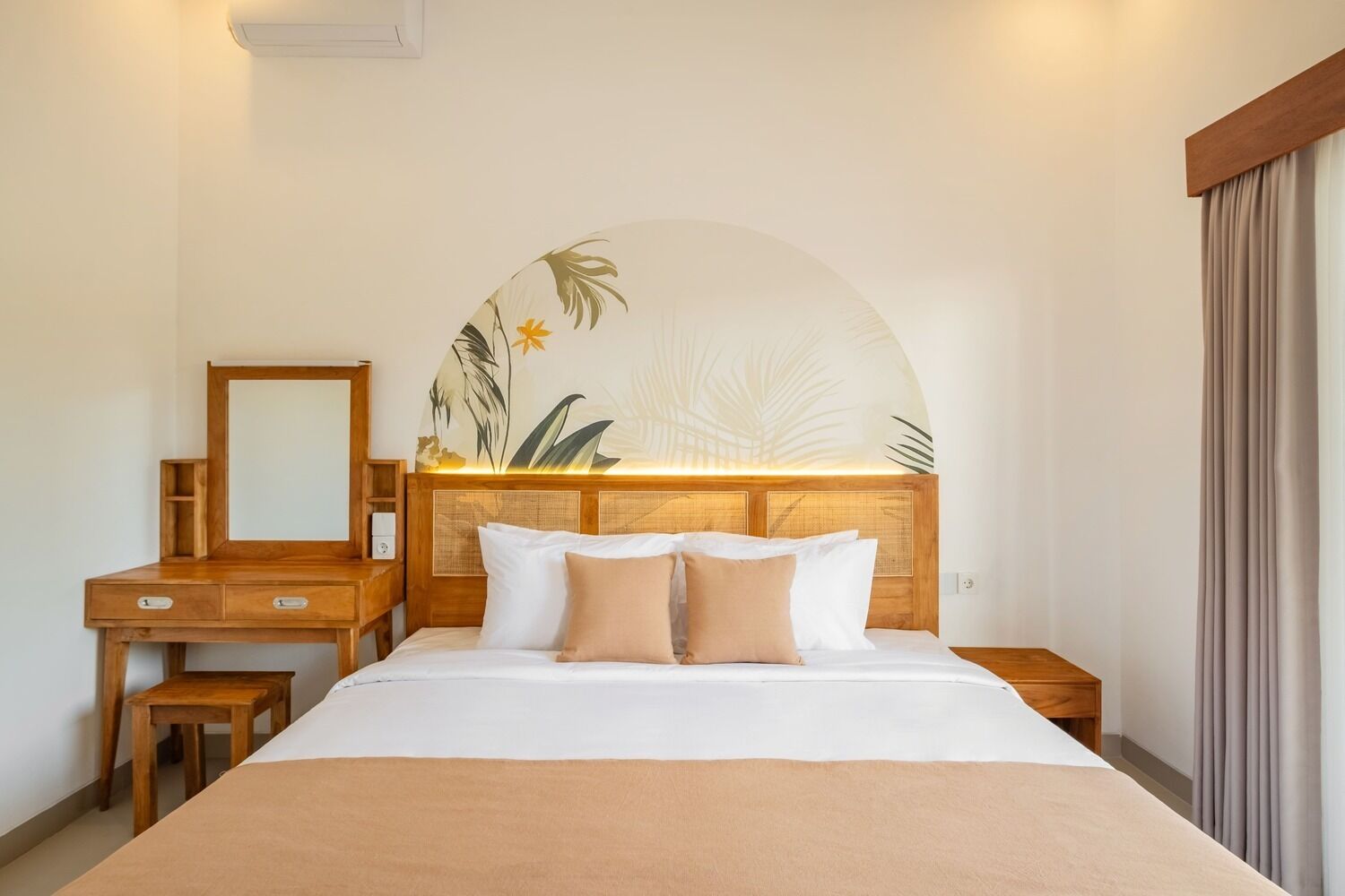 A hotel room with a bed, a wooden desk, a mirror, and a wall-mounted artwork.