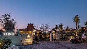 L’entrée d’un hôtel, avec une enseigne indiquant « Cove », une allée pavée, une moto et un palmier.