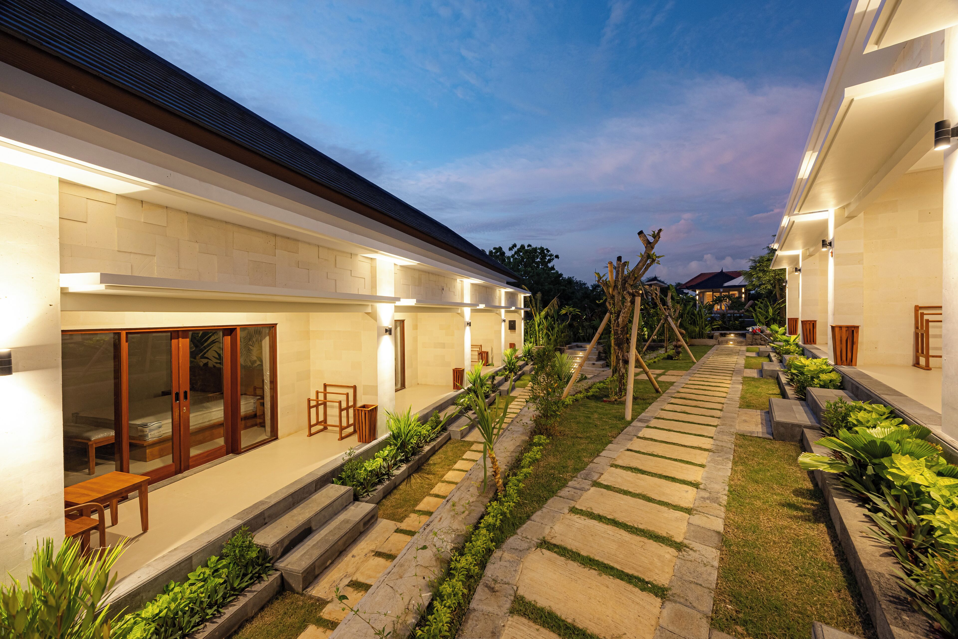 A modern hotel with a well-lit exterior, a central garden pathway, and a series of rooms with large windows.