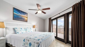 A hotel room with a bed, a ceiling fan, a window with curtains, a nightstand, and a wall-mounted lamp.