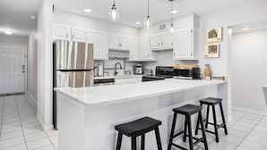A modern kitchen with white cabinets, stainless steel appliances, and black bar stools.