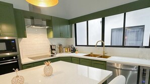 A modern kitchen with green cabinets, white countertops, and stainless steel appliances.