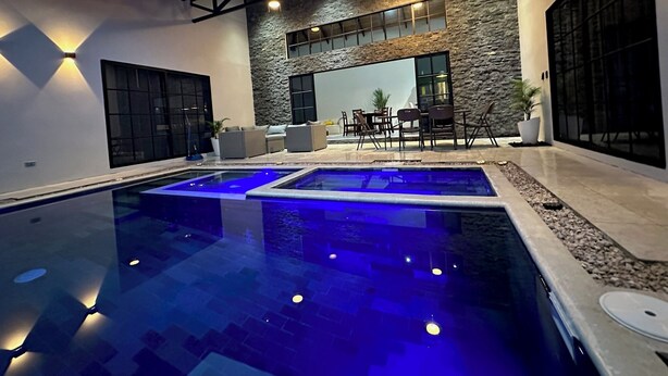 A modern outdoor pool area with two separate pools, stone walls, and a seating area with chairs and a table.