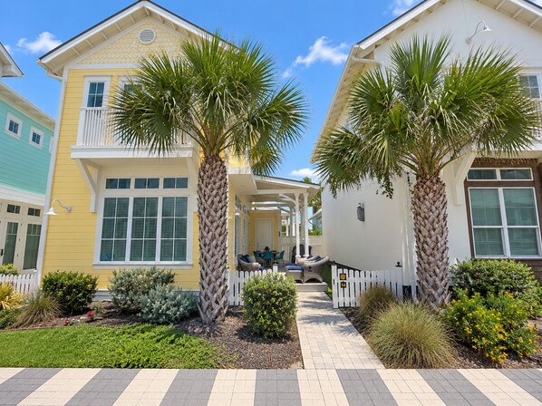 A row of colorful houses with palm trees, a covered patio, and a white picket fence.