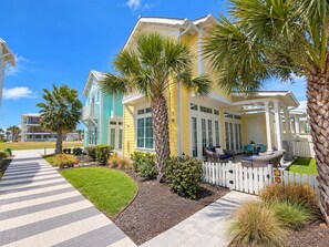 A multi-story residential building with a covered patio area, palm trees, and a paved walkway. - Resort Pools, Golf Cart Boardwalk to the Beach, Pet Friendly (Port Aransas)