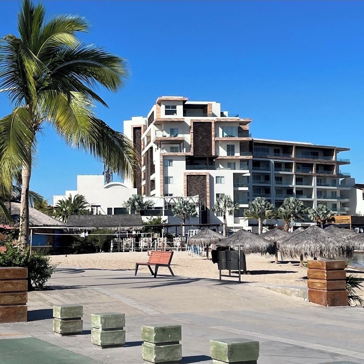 A modern hotel with multiple floors, a pool area with lounge chairs, and palm trees.
