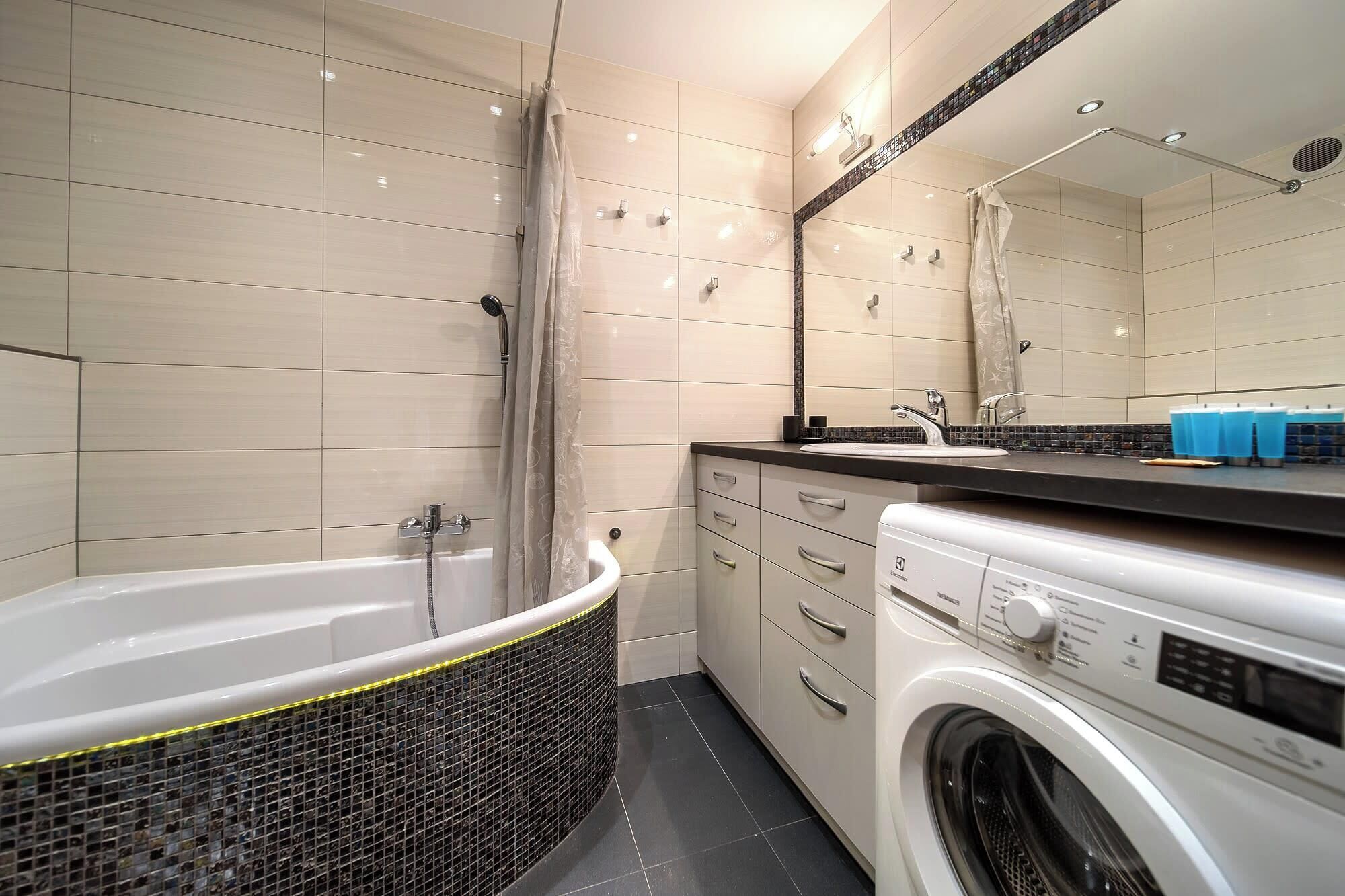 A modern bathroom with a bathtub, a washing machine, and a sink with a mirror above.