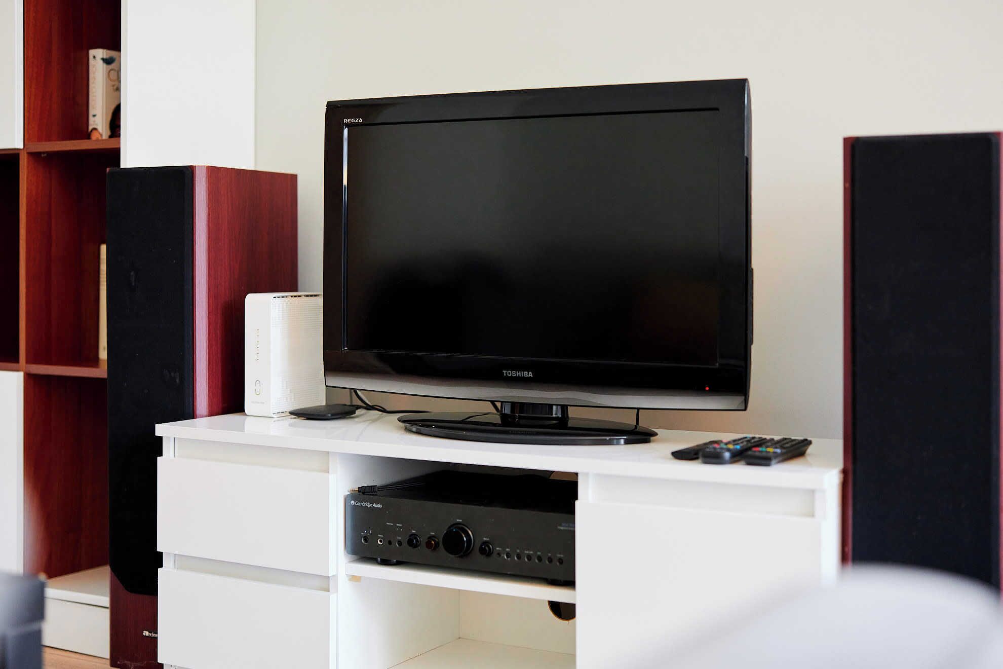A flat-screen TV on a white entertainment unit with a subwoofer, a Cambridge Audio device, and a remote control.
