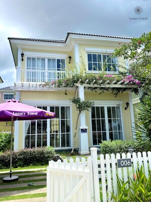 A two-story building with a balcony, a white picket fence, and a purple umbrella with "Luxury Travel" branding.