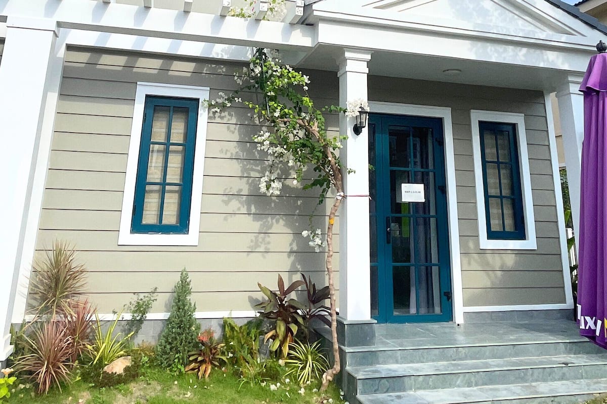 A two-story house with a front porch, a blue door, and a small garden with various plants.