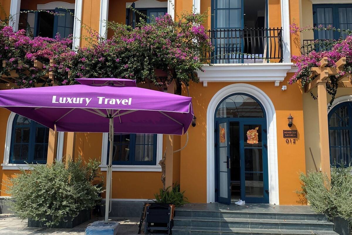 A building with a yellow facade, a balcony with a black railing, and a purple umbrella labeled "Luxury Travel".