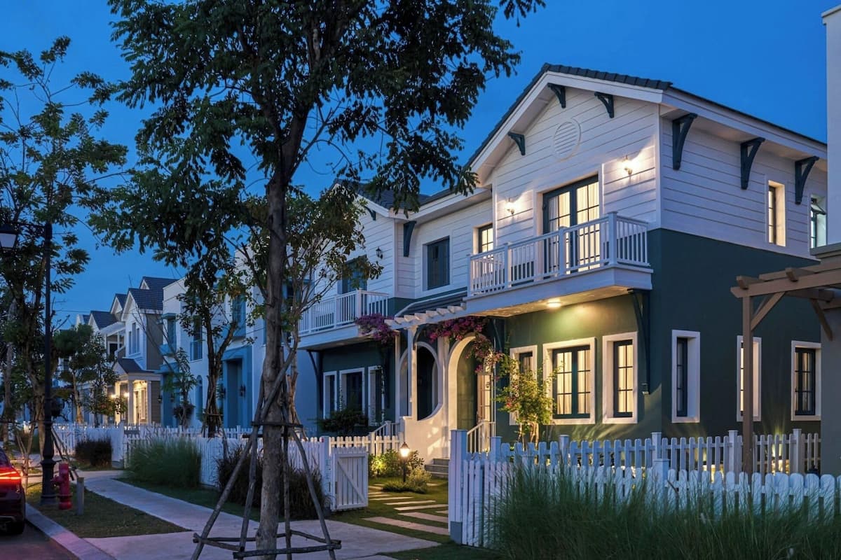 A two-story house with a balcony, white picket fence, and a driveway.