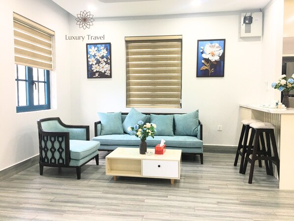 A modern living room with a sofa, two armchairs, a coffee table, and a kitchen area with stools. - Nova Beachfront Haven Villa By An Gia Hospitality (Tien Thanh)