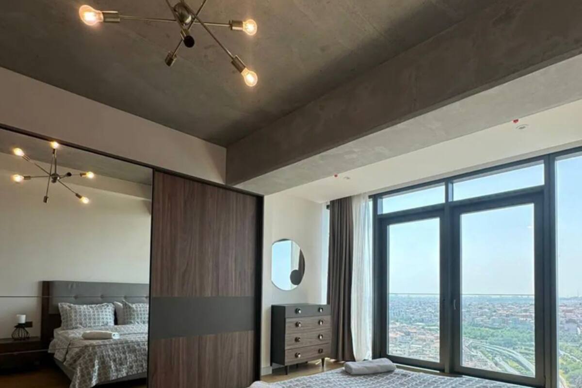 Une chambre moderne avec un grand lit, un miroir, une commode et une vue sur la ville.