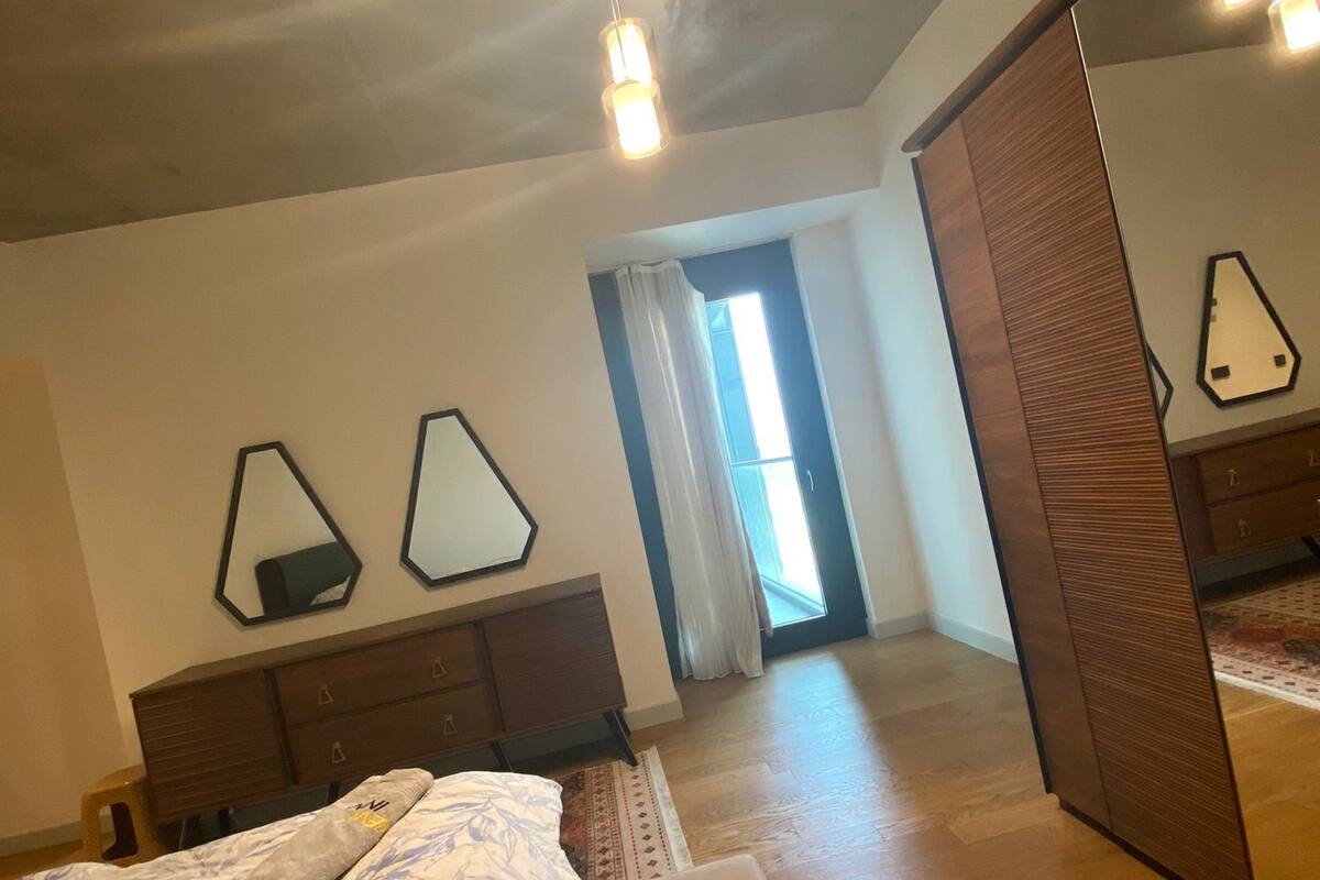 Une chambre à coucher comprenant un lit, une armoire en bois, un miroir et un luminaire fixé au plafond.