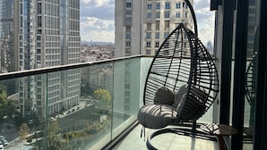 A balcony with a hanging chair, a glass railing, and a city view. - Sinpas Queen Bomonti Residence By Bondy (Istanbul)