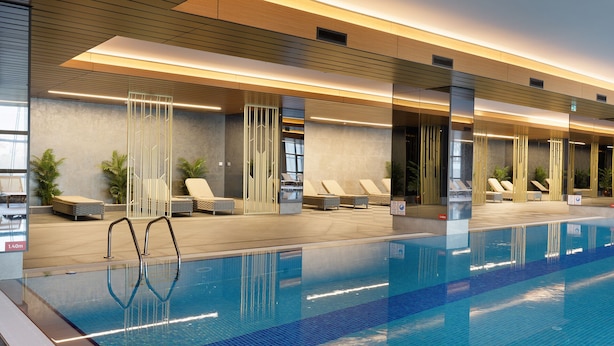 A modern indoor swimming pool with lounge chairs and a sunbed area, surrounded by wooden paneling and glass partitions. - Sinpas Queen Bomonti Residence By Bondy (Istanbul)