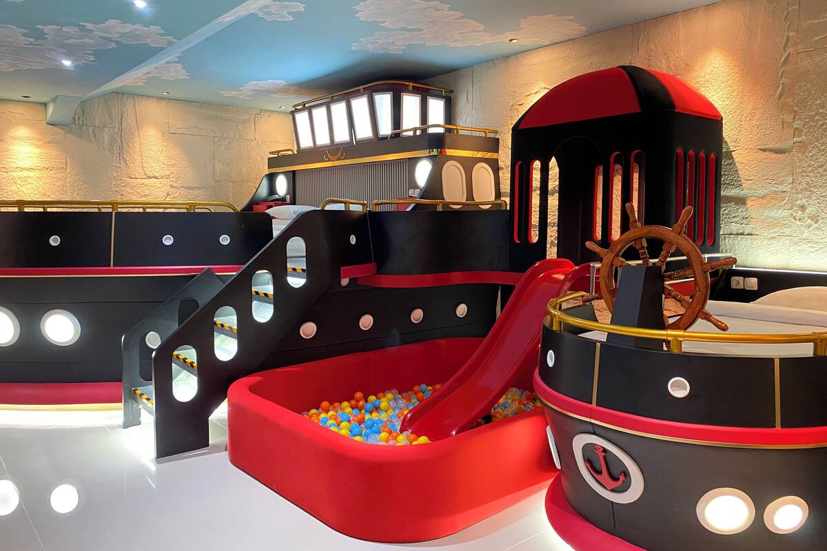 Un espace de jeux pour enfants avec un toboggan et une piscine à balles, conçu pour ressembler à un navire, avec un volant de capitaine.