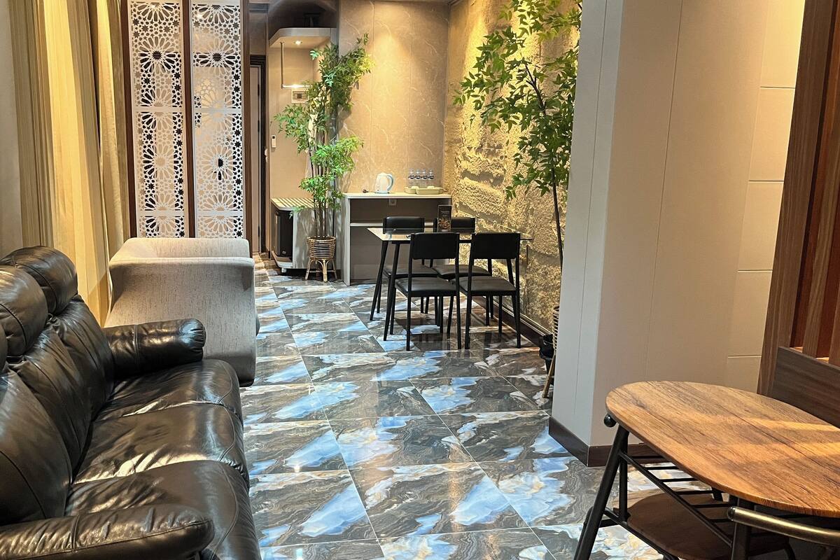 Un salon moderne avec un canapé en cuir, un coin repas comprenant une table et des chaises, et une plante décorative.