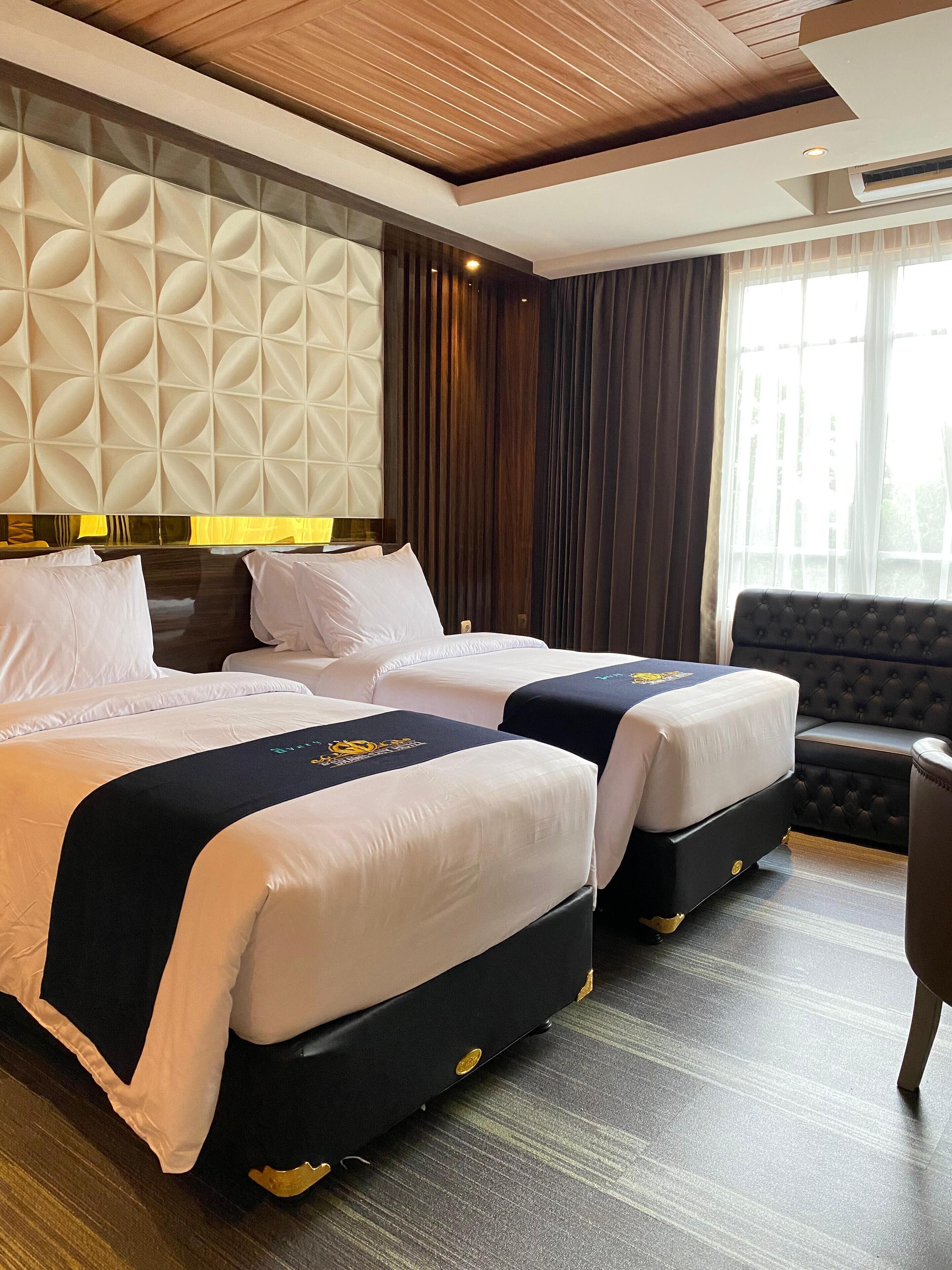 A hotel room with two beds, a dark upholstered sofa, a wooden ceiling, and a large window with curtains.