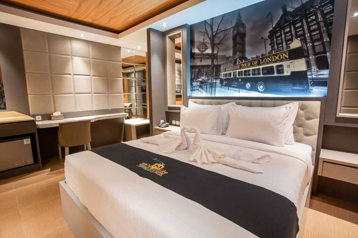 Une chambre d’hôtel avec un grand lit, un bureau et une chaise. Un poster représentant un circuit touristique de Londres est accroché au mur.