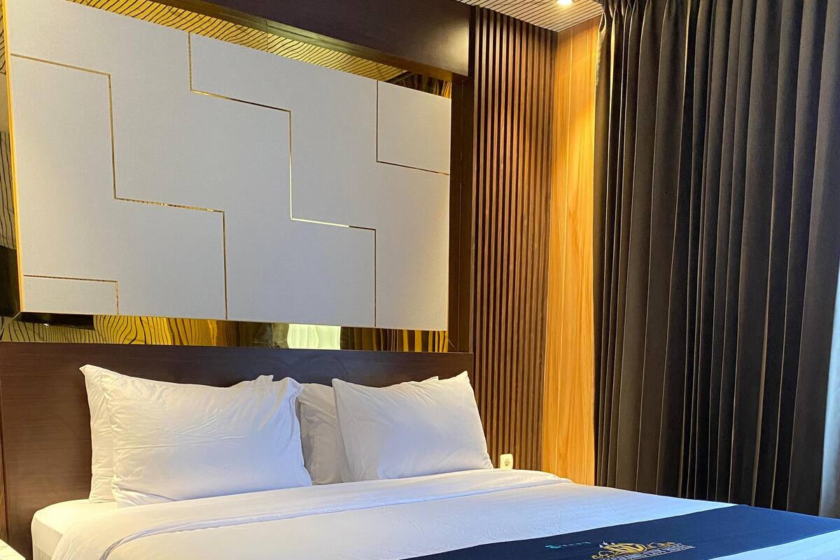 Une chambre d’hôtel avec un grand lit, une tête de lit ornée de motifs géométriques, un rideau foncé et un panneau mural en bois.