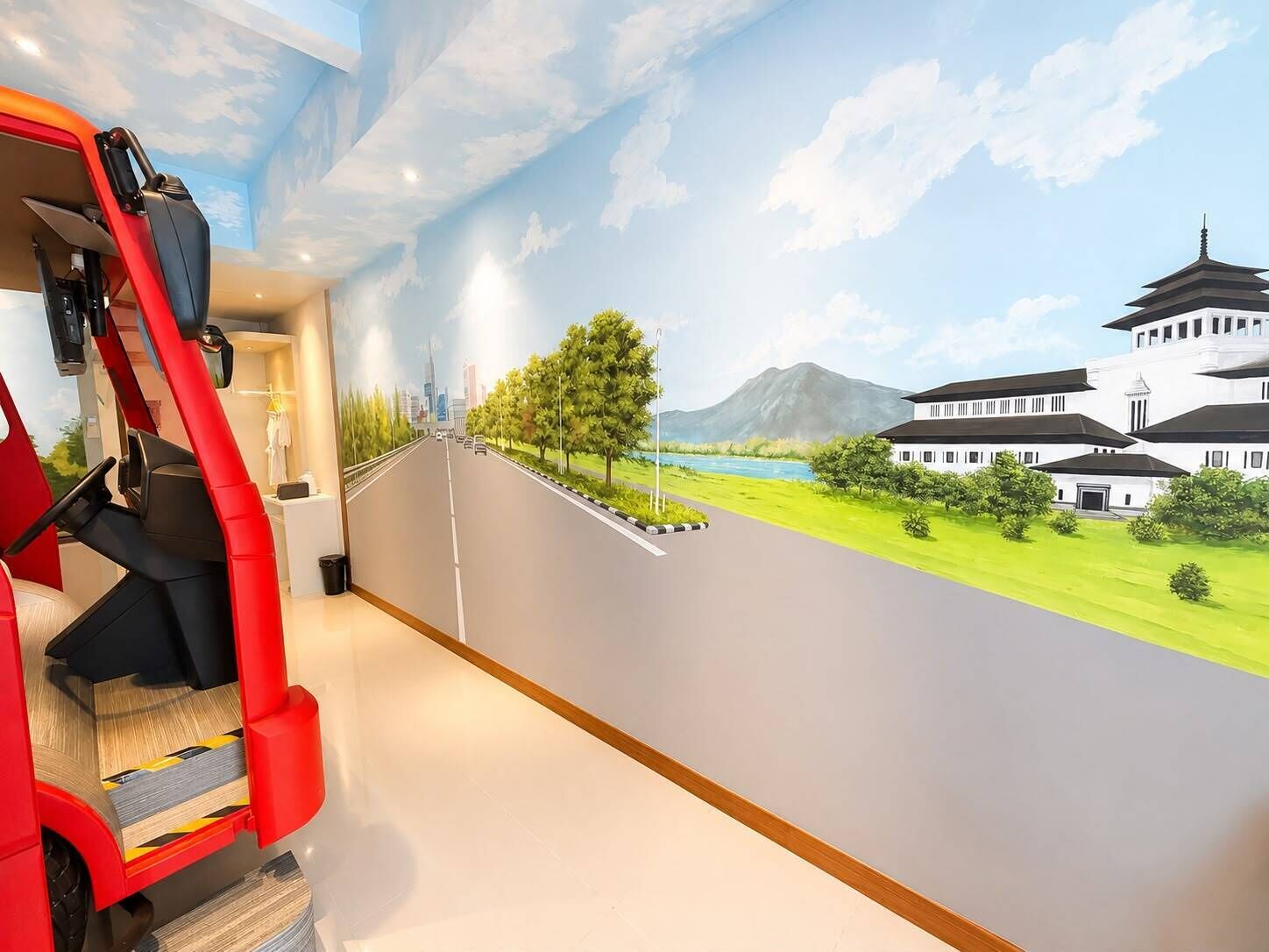 Habitación con un mural que muestra un camino que lleva a una construcción tradicional, una silla roja y una pequeña mesa.