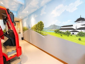 A room with a mural of a road leading to a traditional building, a red chair, and a small table.