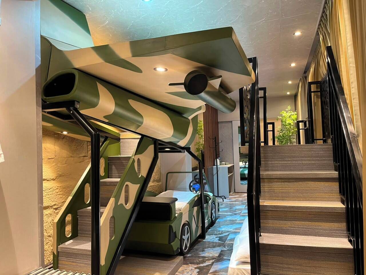 A staircase with a unique camouflage design, a vehicle integrated into the structure, and a modern interior with a stone wall and a plant.
