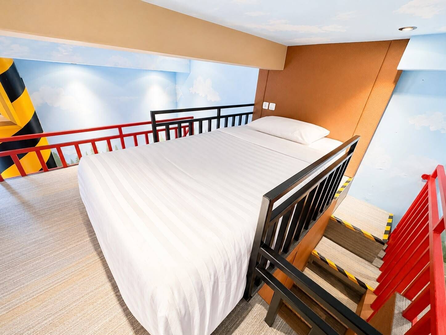 A bedroom with a bed, a red railing, and a mural of a sky and mountains.