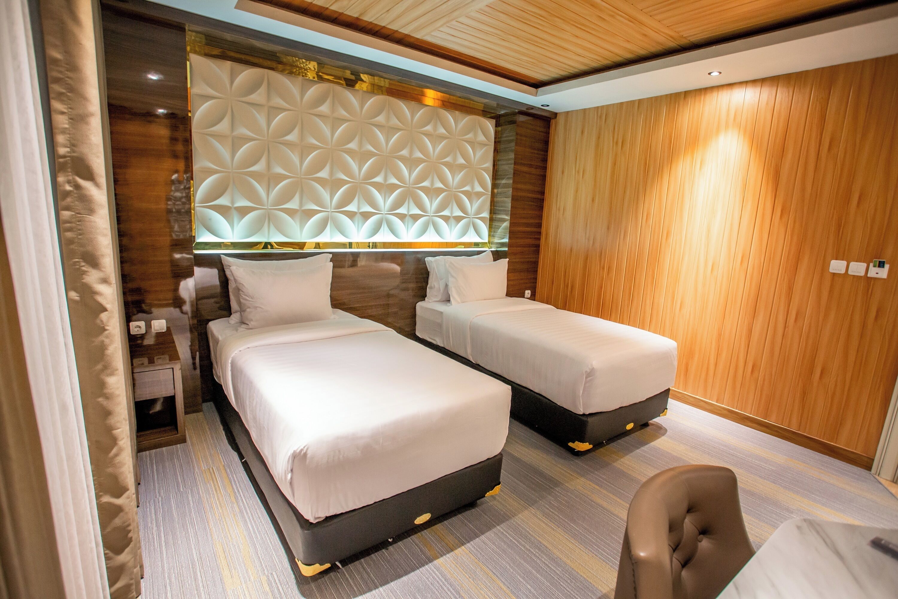 A hotel room with two beds, a wooden headboard, a small desk, and a chair.